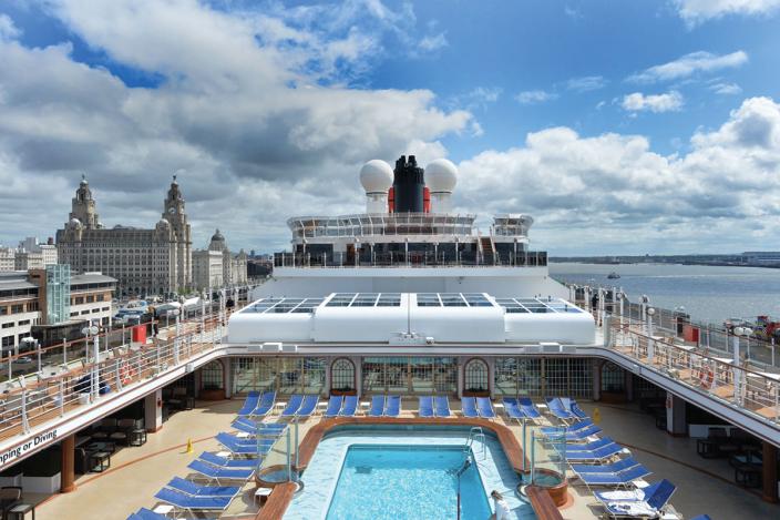 view on board a cruise vessel looking across at the on board pool and deck chairs with the royal liver building in the background