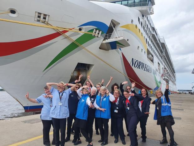 a group of ladies in cruise liverpool blue uniform cheering in front of a ship